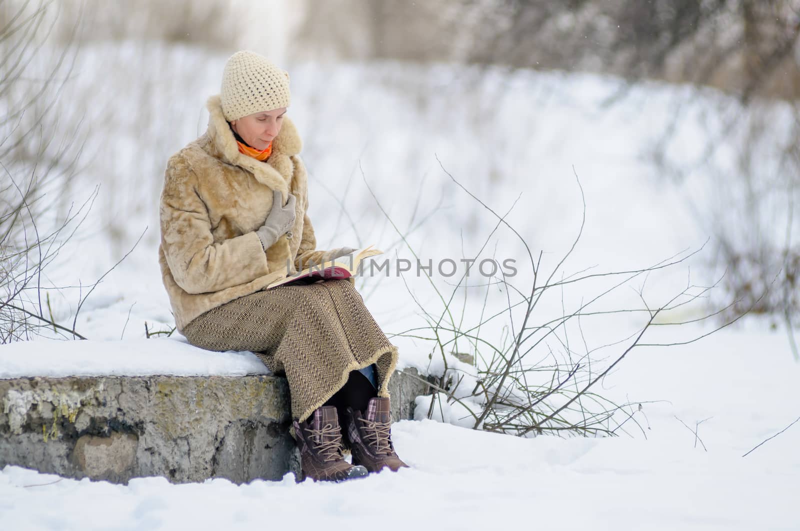 Woman sitting on a bench and reading a book in winter. Snow.