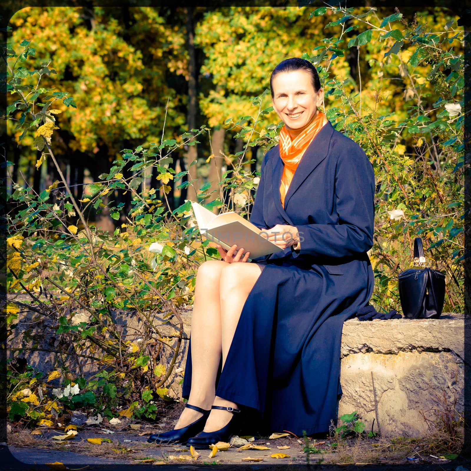 Sexy senior woman reading a book in the park during a sunny autumn day