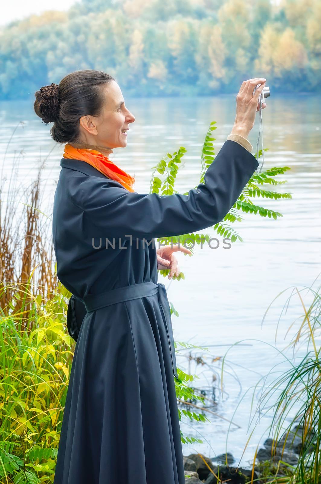 Elegant senior business woman with a digital camera, a bag and an orange scarf, taking pictures along the river