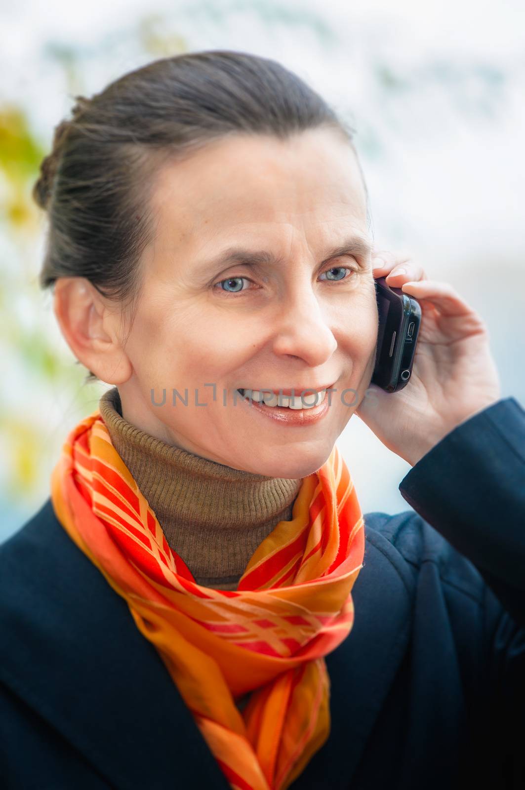 Portrait of an elegant senior business woman with a mobile phone, and an orange scarf, under the trees in autumn