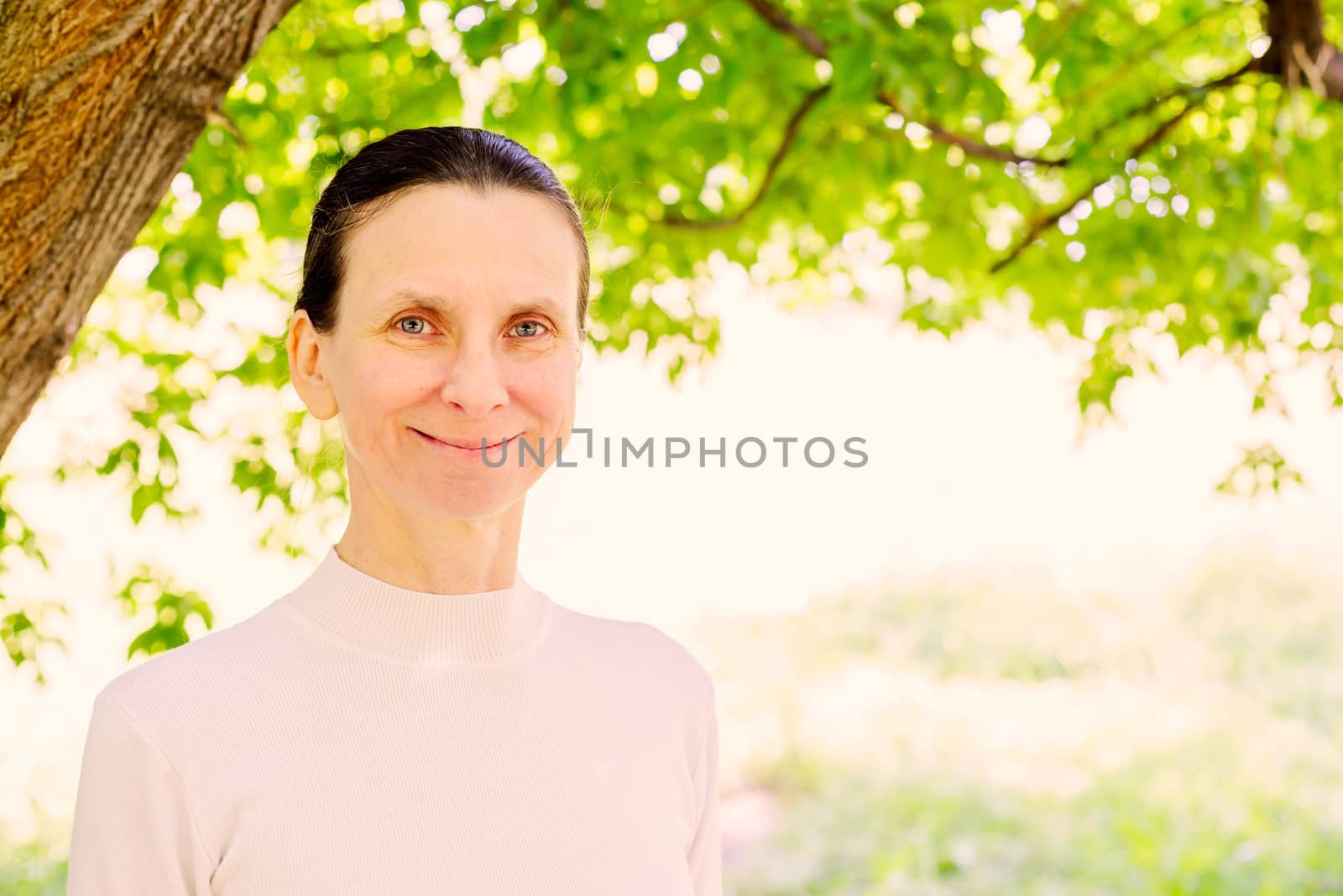 A warm portrait of a nice smiling senior woman in the park under a tree in summer