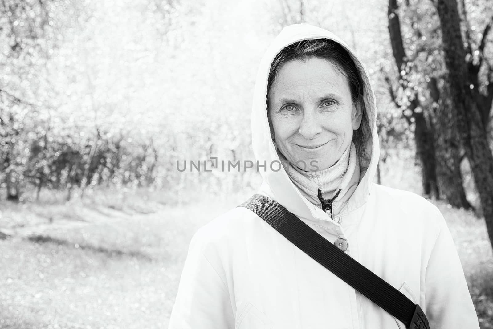 Black and white high-key portrait of a happy adult woman wearing a coat with a hood and smiling with a warm and positive expression