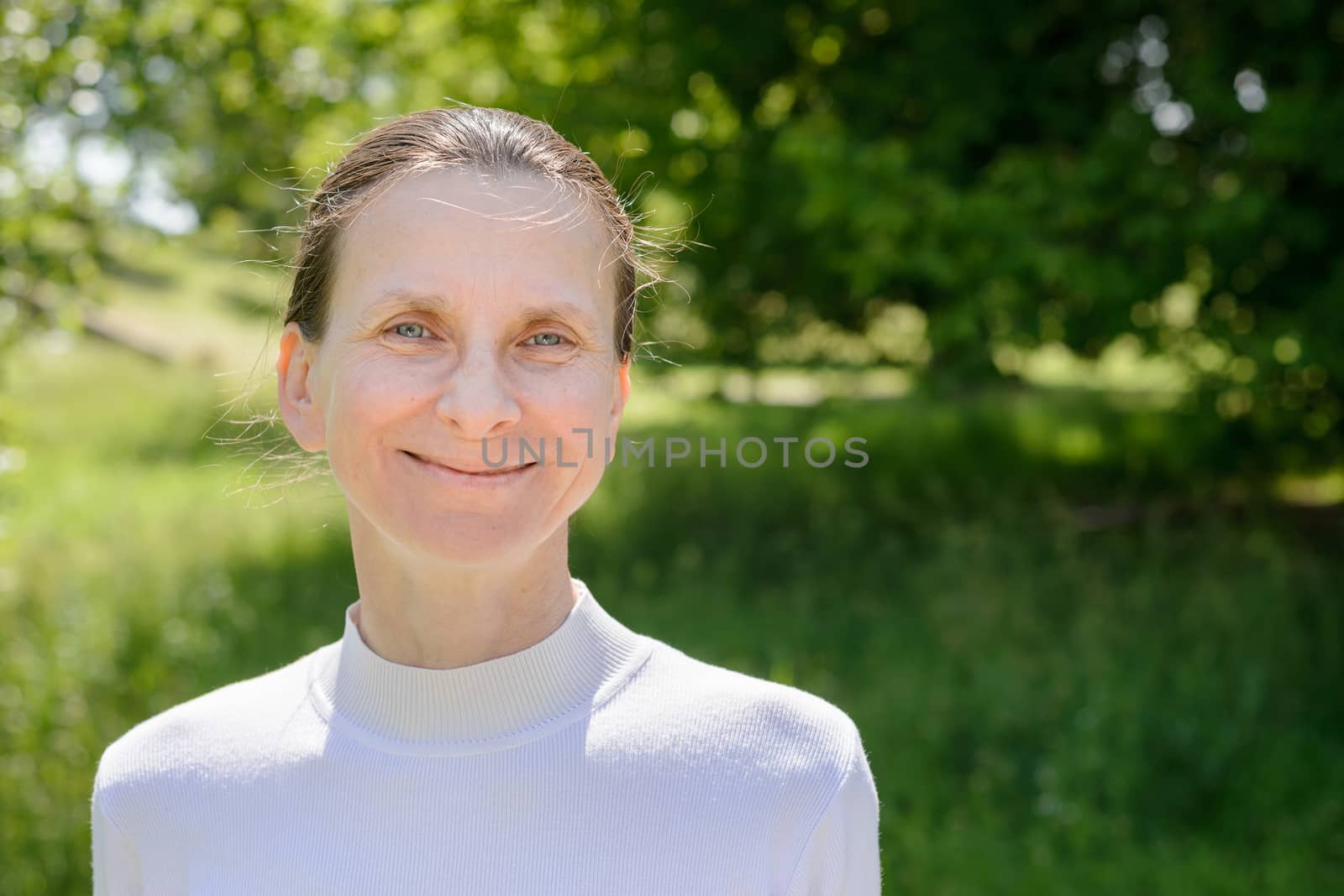 A warm portrait of a nice smiling senior woman in the park under the warm summer sun