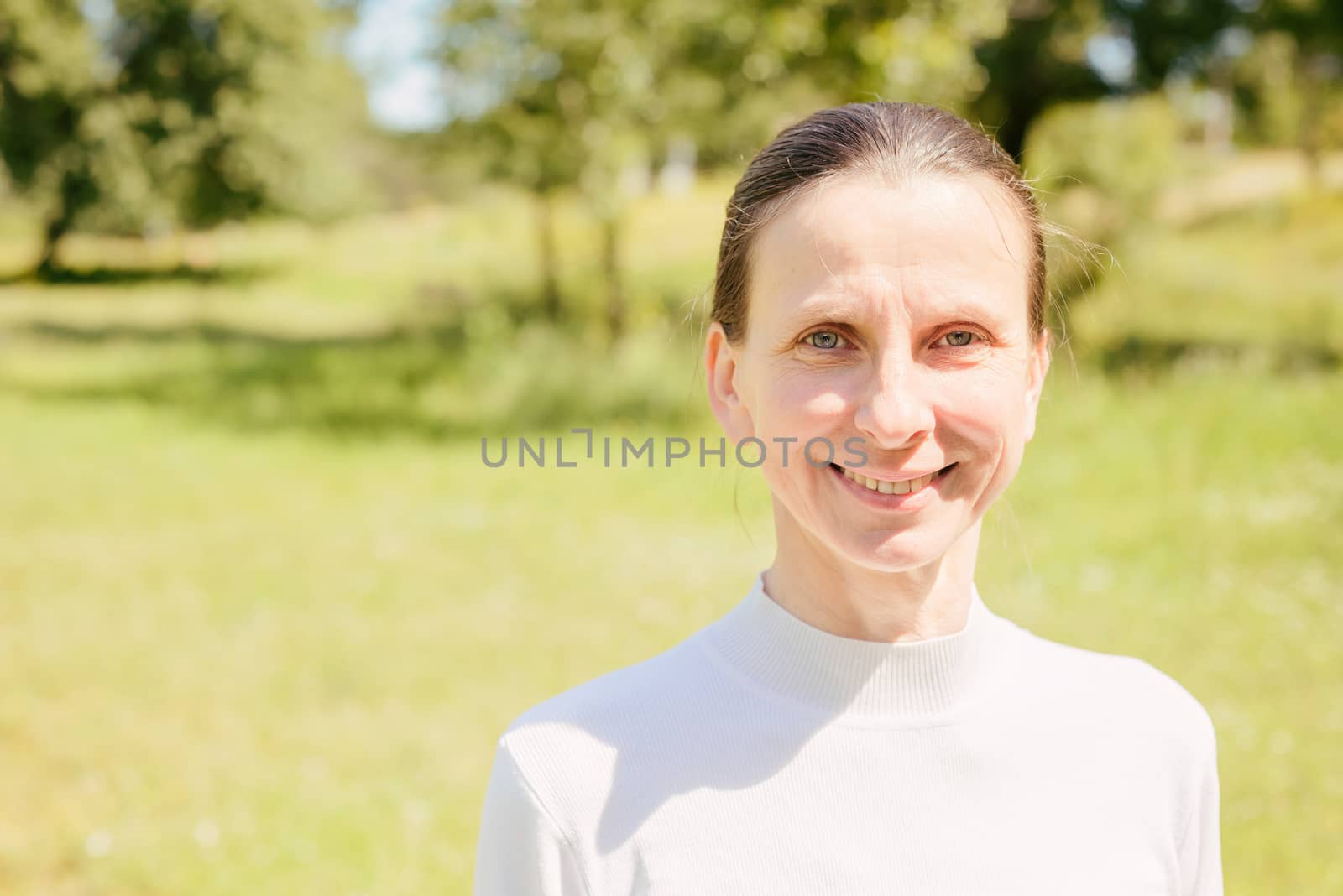 A warm portrait of a nice smiling senior woman in the park under the warm summer sun