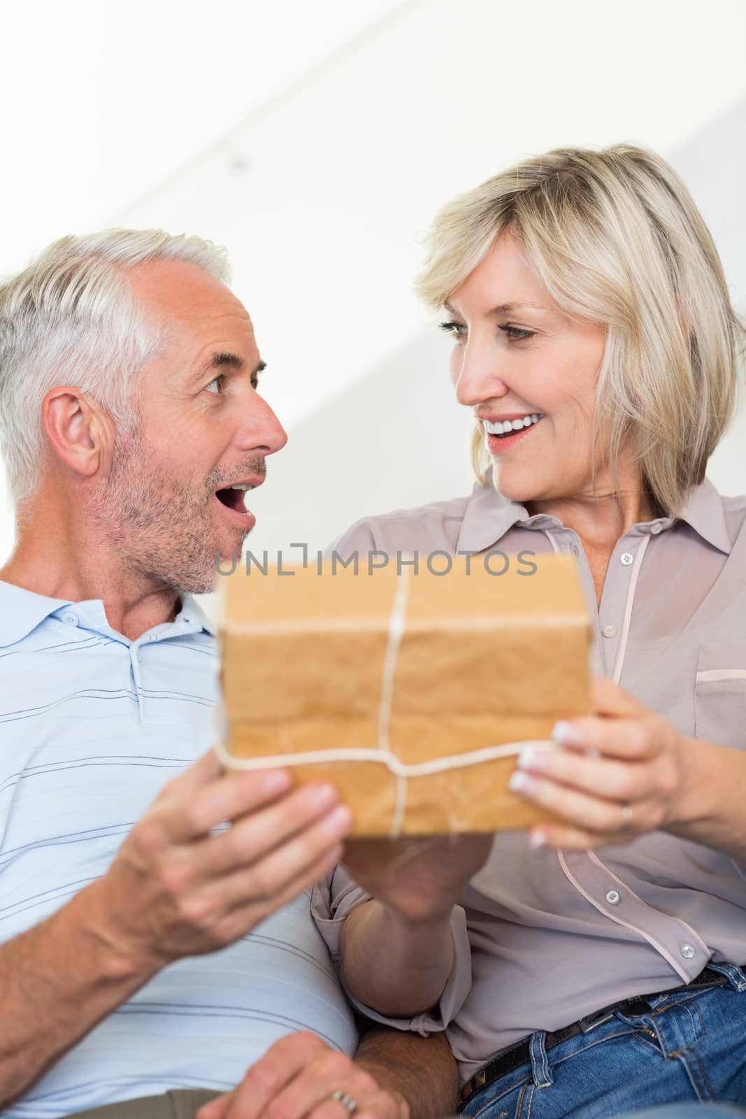 Portrait of a smiling woman surprising mature man with a gift on sofa at home