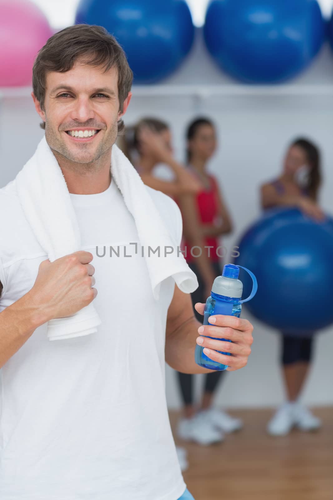 Man holding water bottle with friends in background at fitness studio by Wavebreakmedia