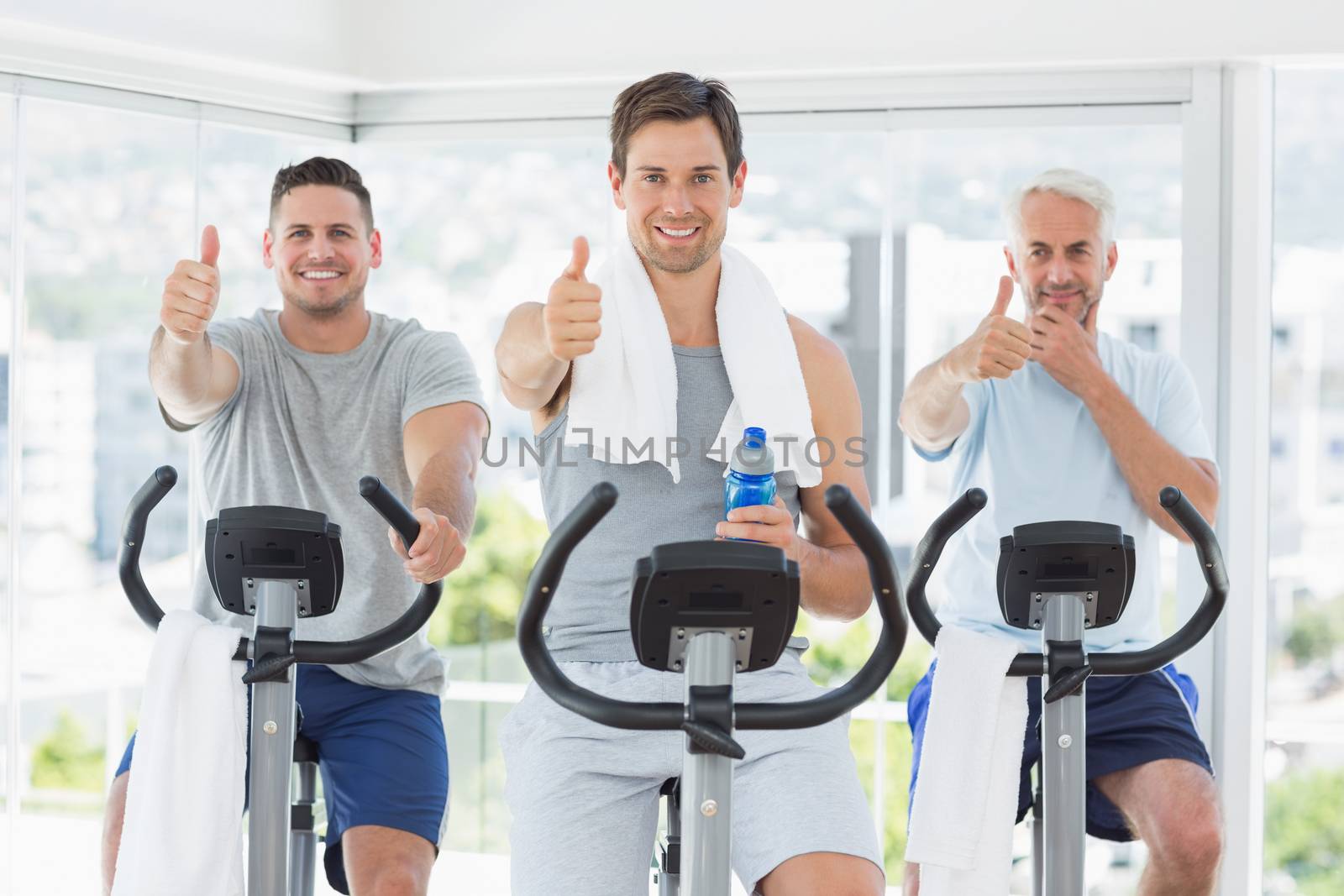 Portrait of men on exercise bikes gesturing thumbs up at gym
