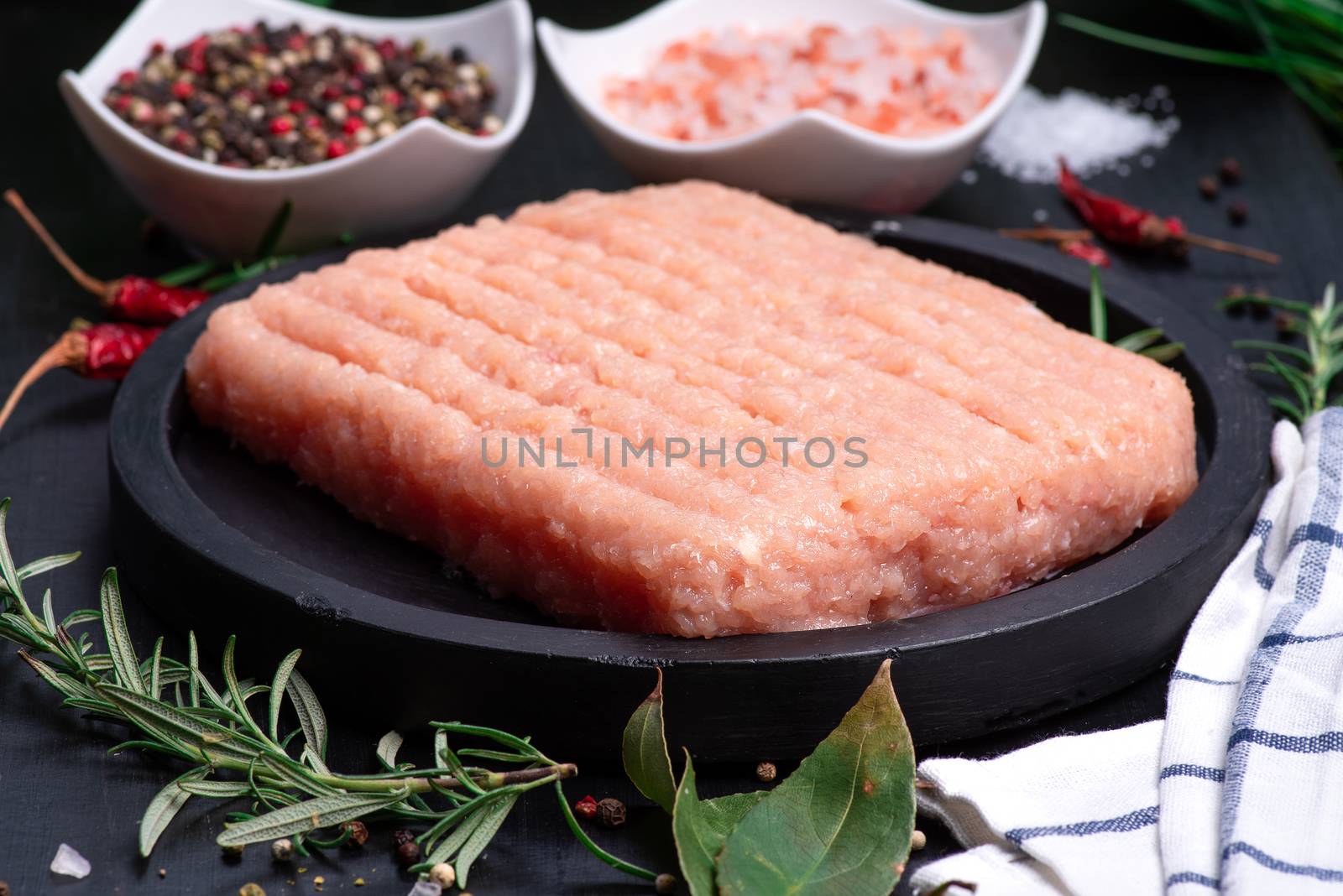 Raw minced chicken on a black plate on a wooden table. Top view. Minced chicken close-up. Raw Minced meat with herbs and spices by nkooume