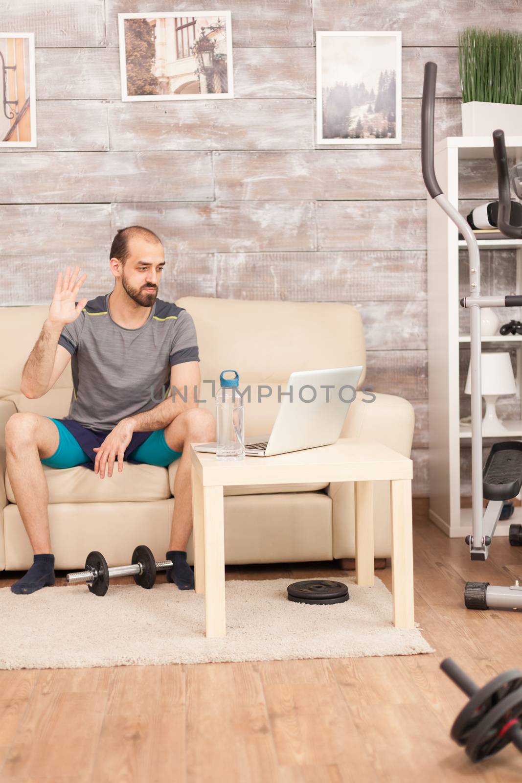 Athletic man waving at his personal trainer during online workout in time of global pandemic.