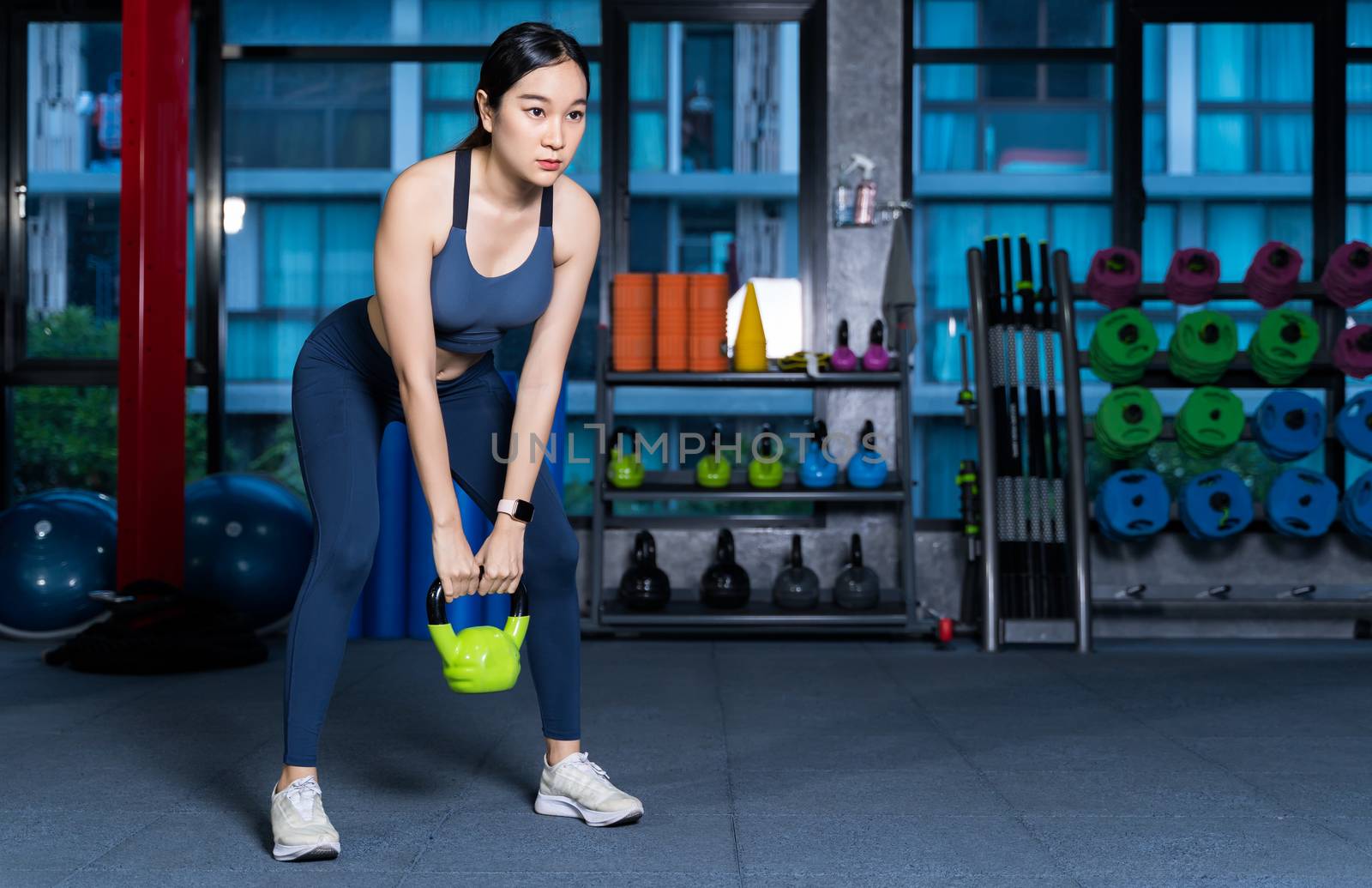 Healthy asian women are doing lifting gear, she's doing weight training exercises with Kettlebell at the fitness or gym with blur Racks Fitness Equipment background in sport and healthy concept