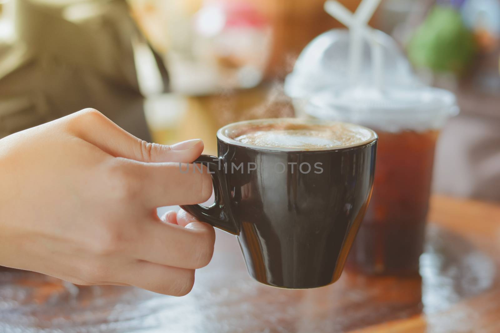 Hold hot coffee, heart shape with milk latte on top of black ceramic cup on hand at coffee shop and cafe in vintage tone, copy space for your text. Times to relax with caffiene concept.