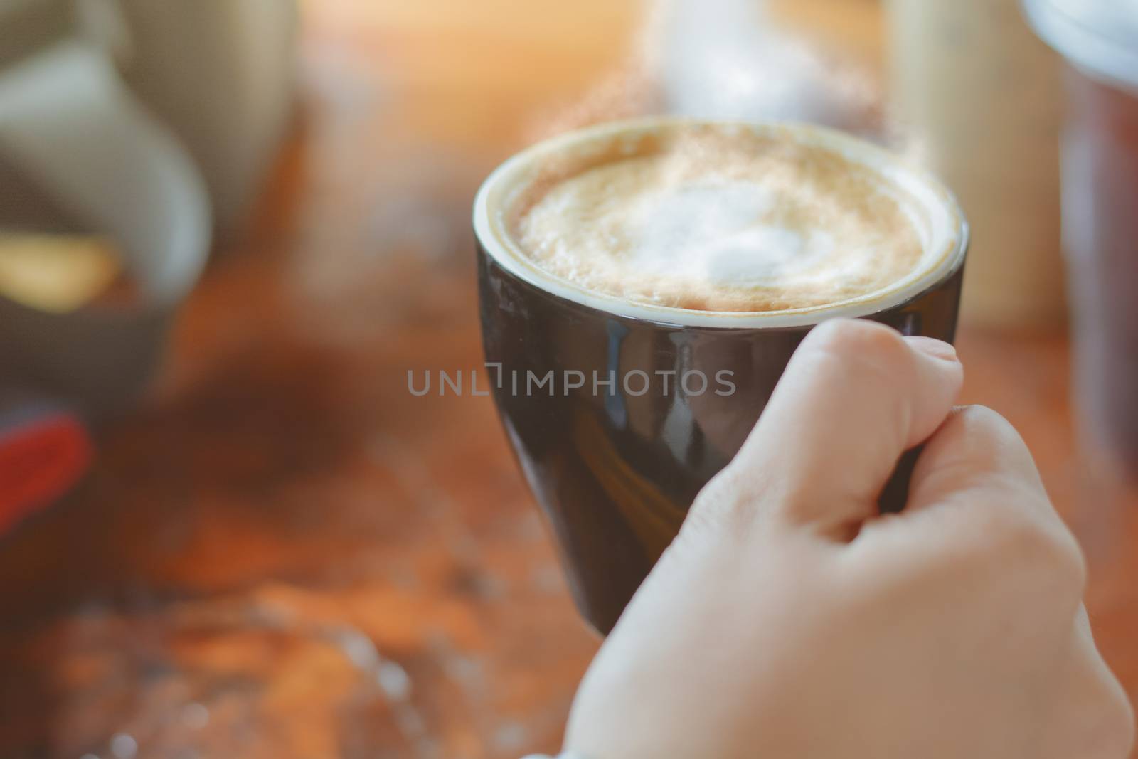 Hold hot coffee, heart shape with milk latte on top of black ceramic cup on hand at coffee shop and cafe in vintage tone, copy space for your text. Times to relax with caffiene concept.