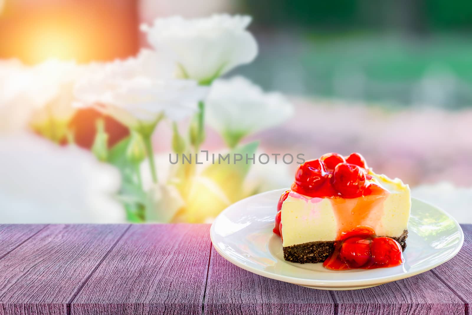 Delicious red cherry cheese pie on a white plate on a wooden table and soft focus of garden background with morning light with copy space for your text. 