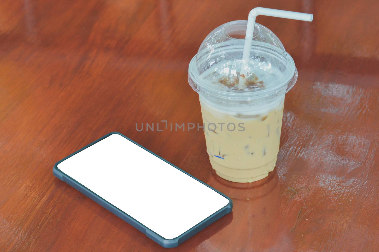 Ice coffee (cappuccino, latte, mocha) in plastic cup and white straw with water drop near smart phone with white screen for your text on brown wooden table in cafe and restaurant. Inconcept time to relax.