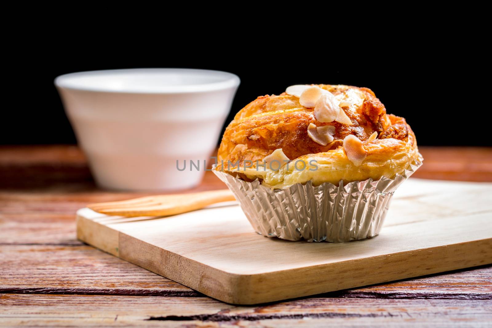 Delicious homemade almond danish bread in foil cup on a wooden chopping board and table in the home kitchen on black background.