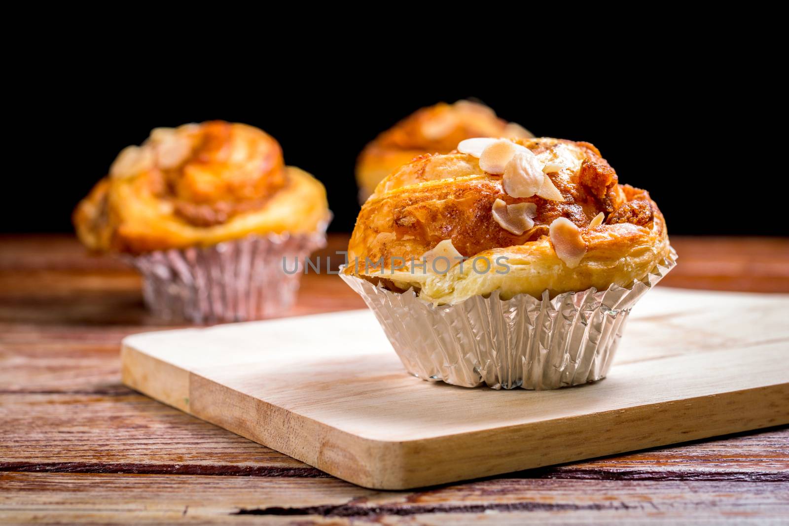 Delicious homemade almond danish bread in foil cup on a wooden chopping board and table in the home kitchen on black background.