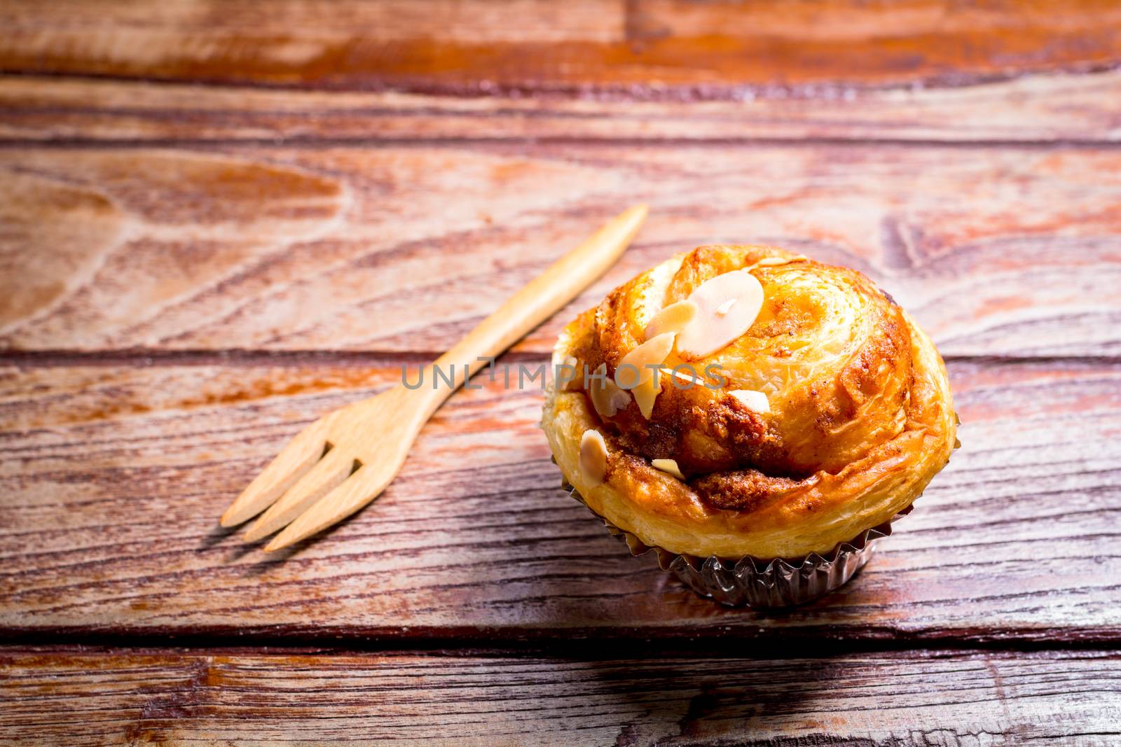 Delicious homemade almond danish bread in foil cup with frok on a wooden table in the home kitchen.