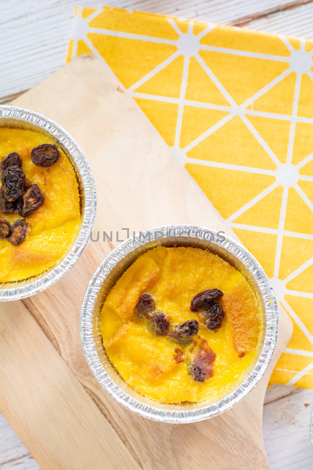 Bread pudding with black rasins in round foil cup on wooden tray. Delicious custard for coffee times.