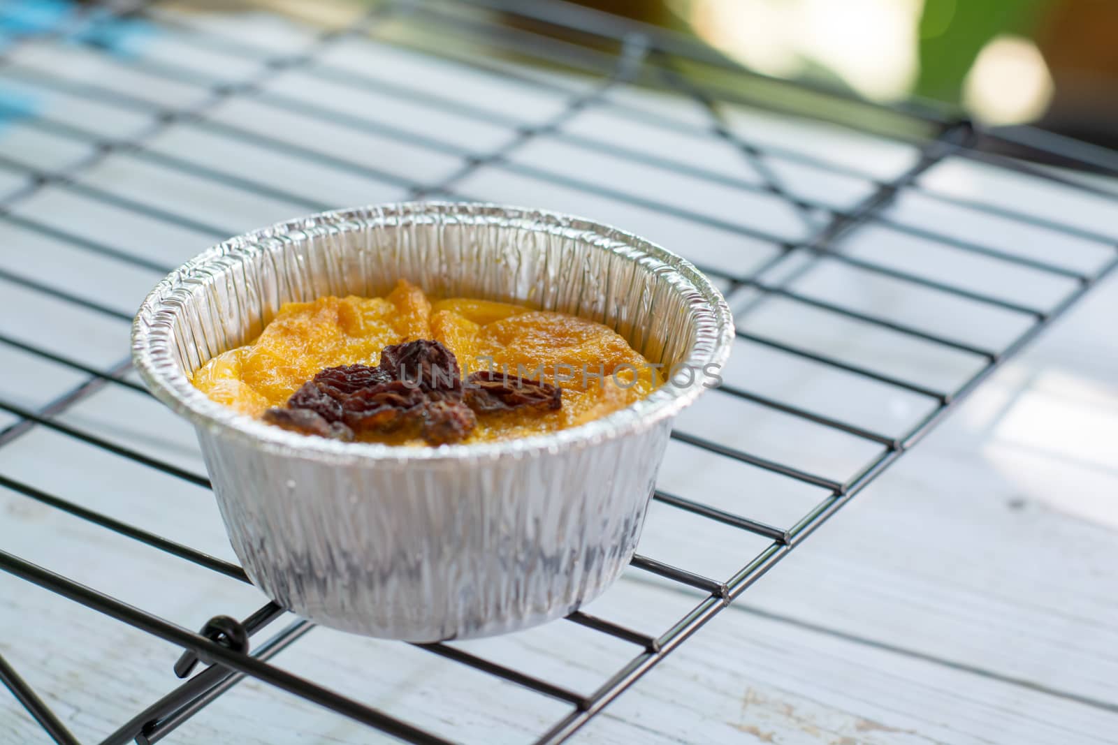 Bread pudding with black rasins in round foil cup on wooden tray. Delicious custard for coffee times.
