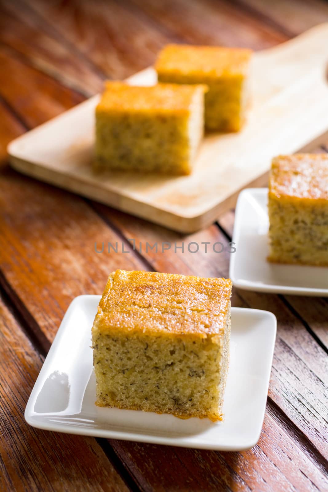 Close up square cut of homemade sweet and solf banana cake on white plate on wooden table. Delicious and healthy bakery.