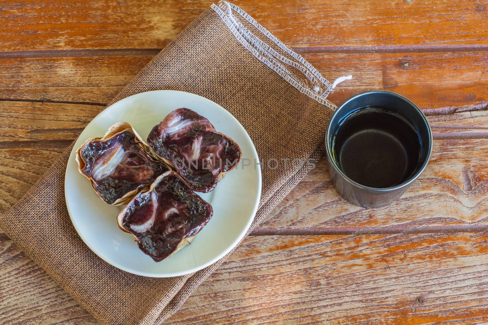 Black sticky rice cake Nian Gao in dried banana leave cup on white plate and wooden table. Traditional snack in Chinese new year.