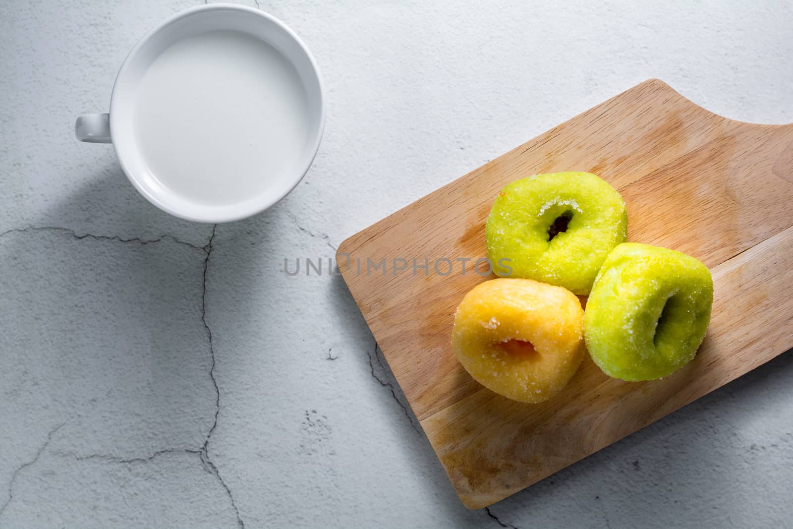 Vanilla and pandan doughnut on wooden chopping board with cup of hot milk. Breakfast concept.