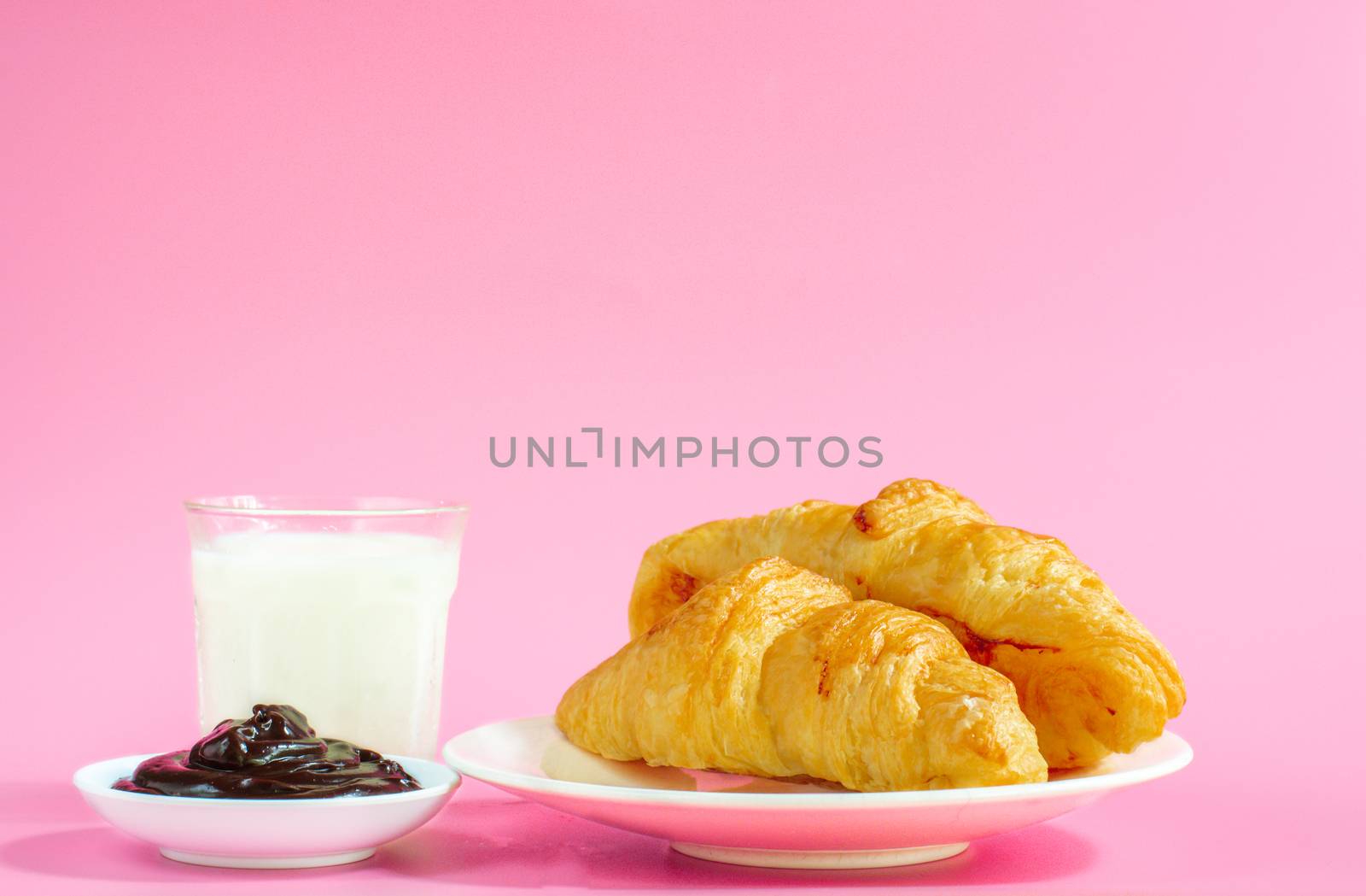 Two croissants on white dish and glass of fresh milk on pink back ground with copy space for your text. Breakfast concept.