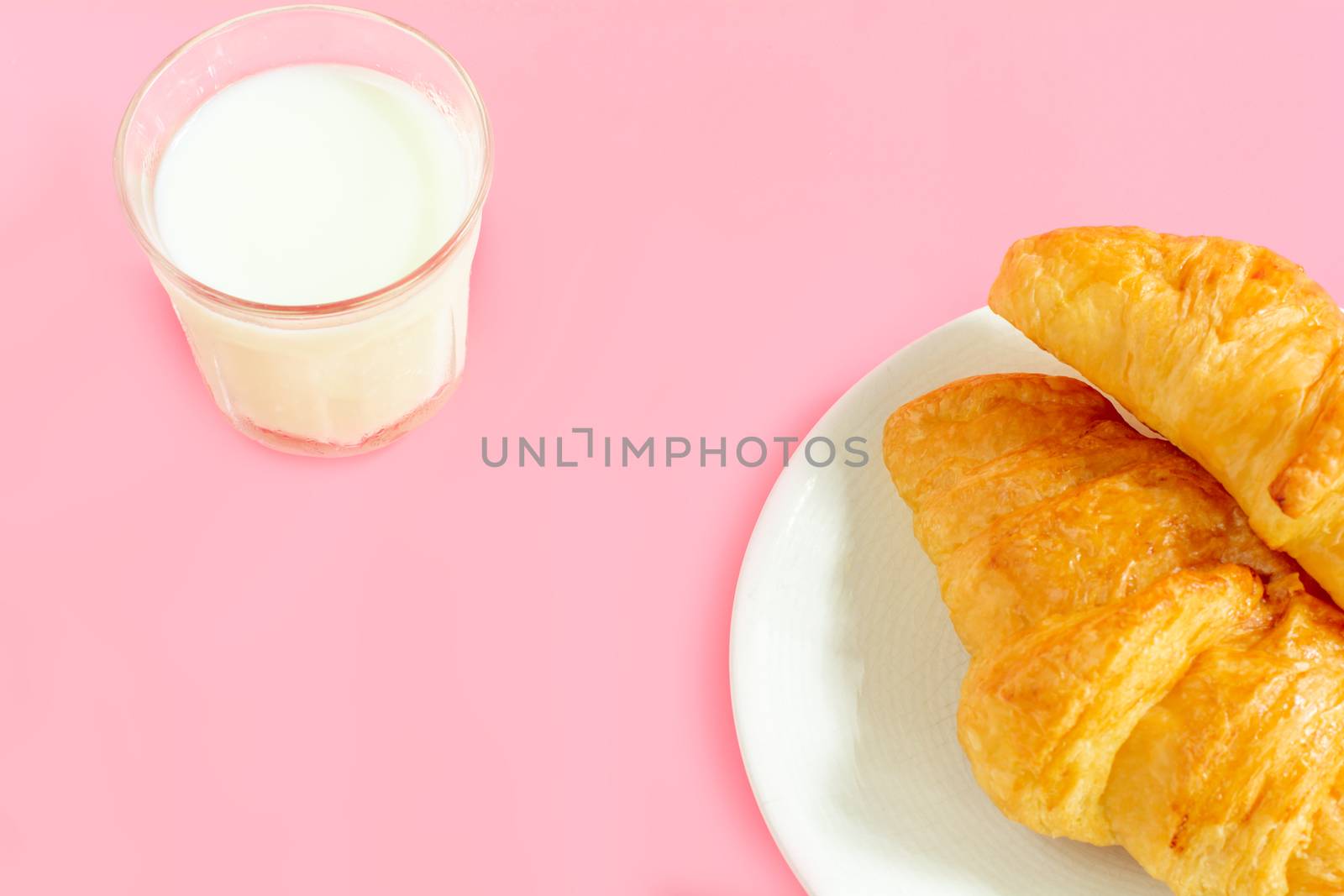 Two croissants on white dish and glass of fresh milk on pink back ground with copy space for your text. Breakfast concept.