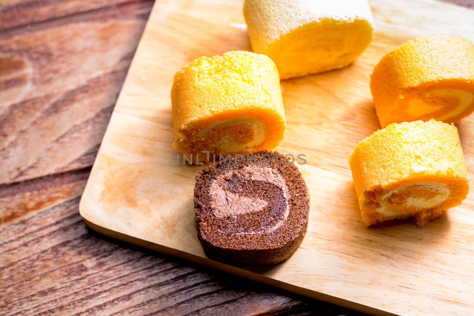 Top view delicious chocolate and orange roll cake with whipping cream on  a wooden chopping board and table at the home kitchen with a black background and copy space. Homemade bakery concept.