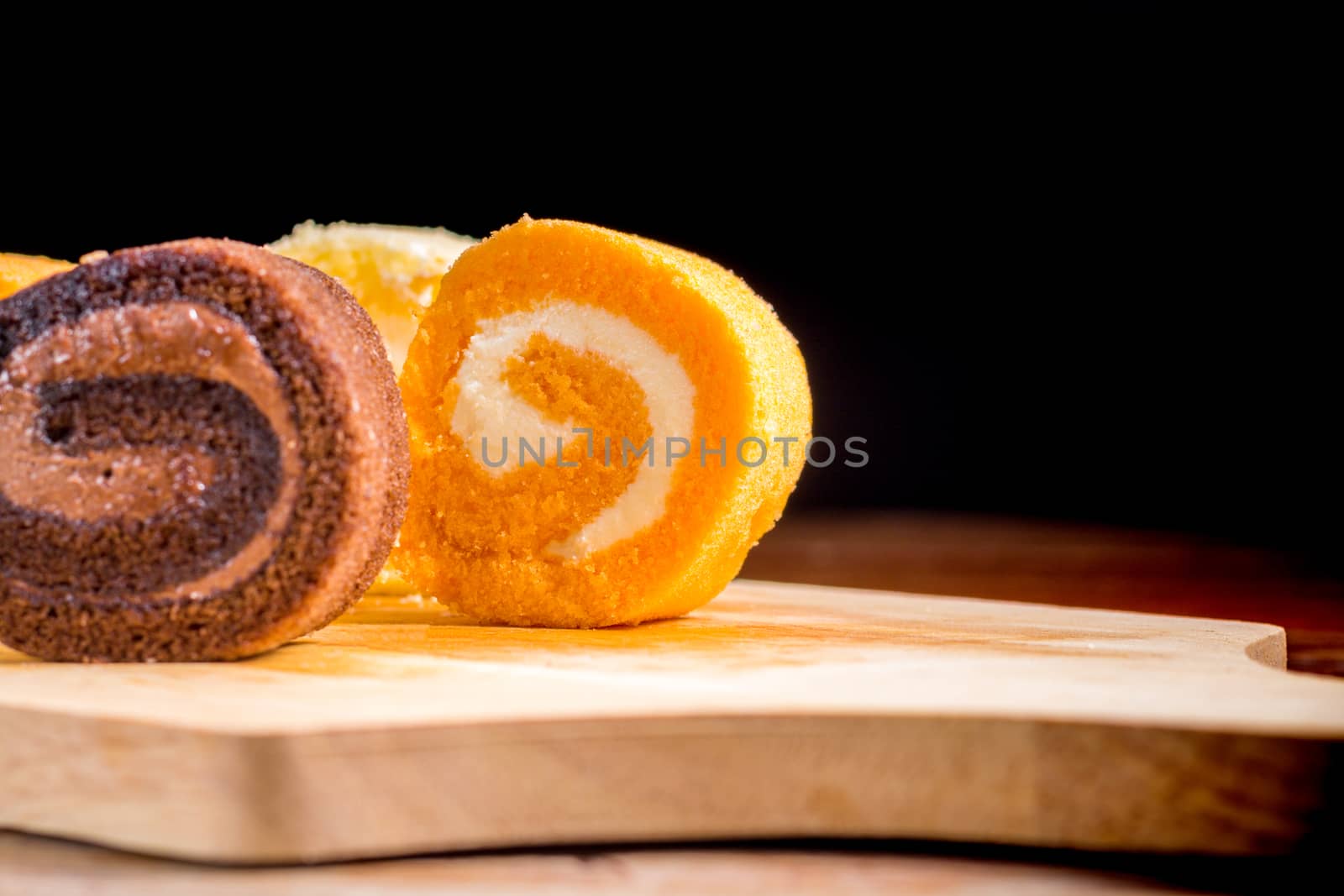 Close up delicious orange roll cake with whipping cream on  a wooden chopping board and table at the home kitchen with a black background and copy space. Homemade bakery concept.