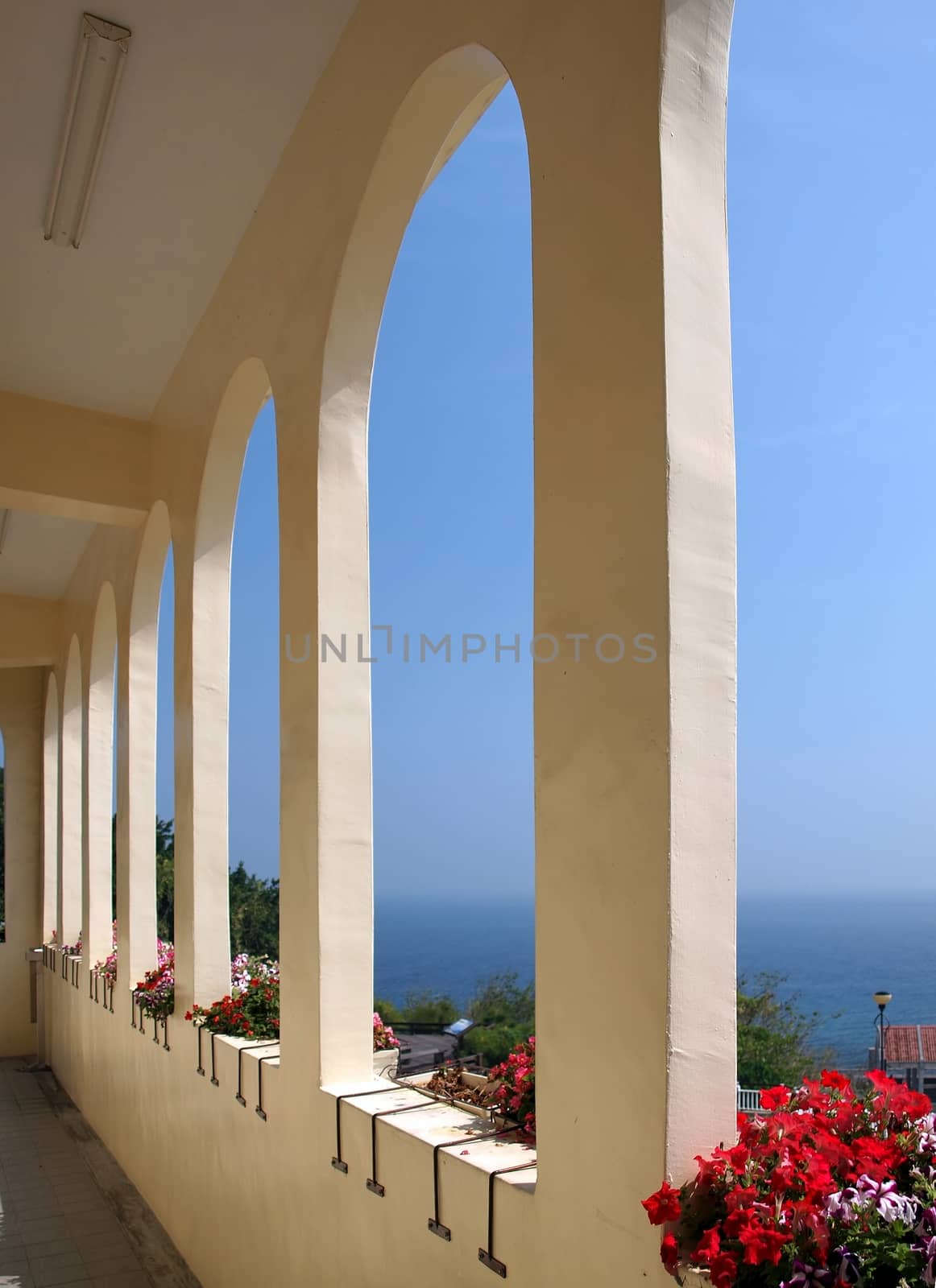 A view of the blue sea through the arches of a colonnade terrace
