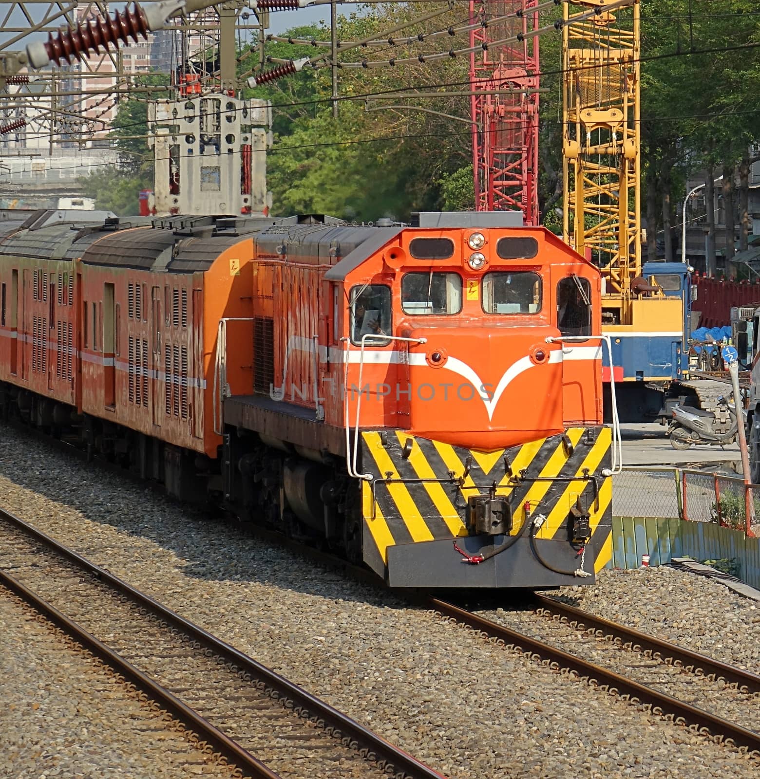 An orange colored diesel engine passes by a large scale construction site