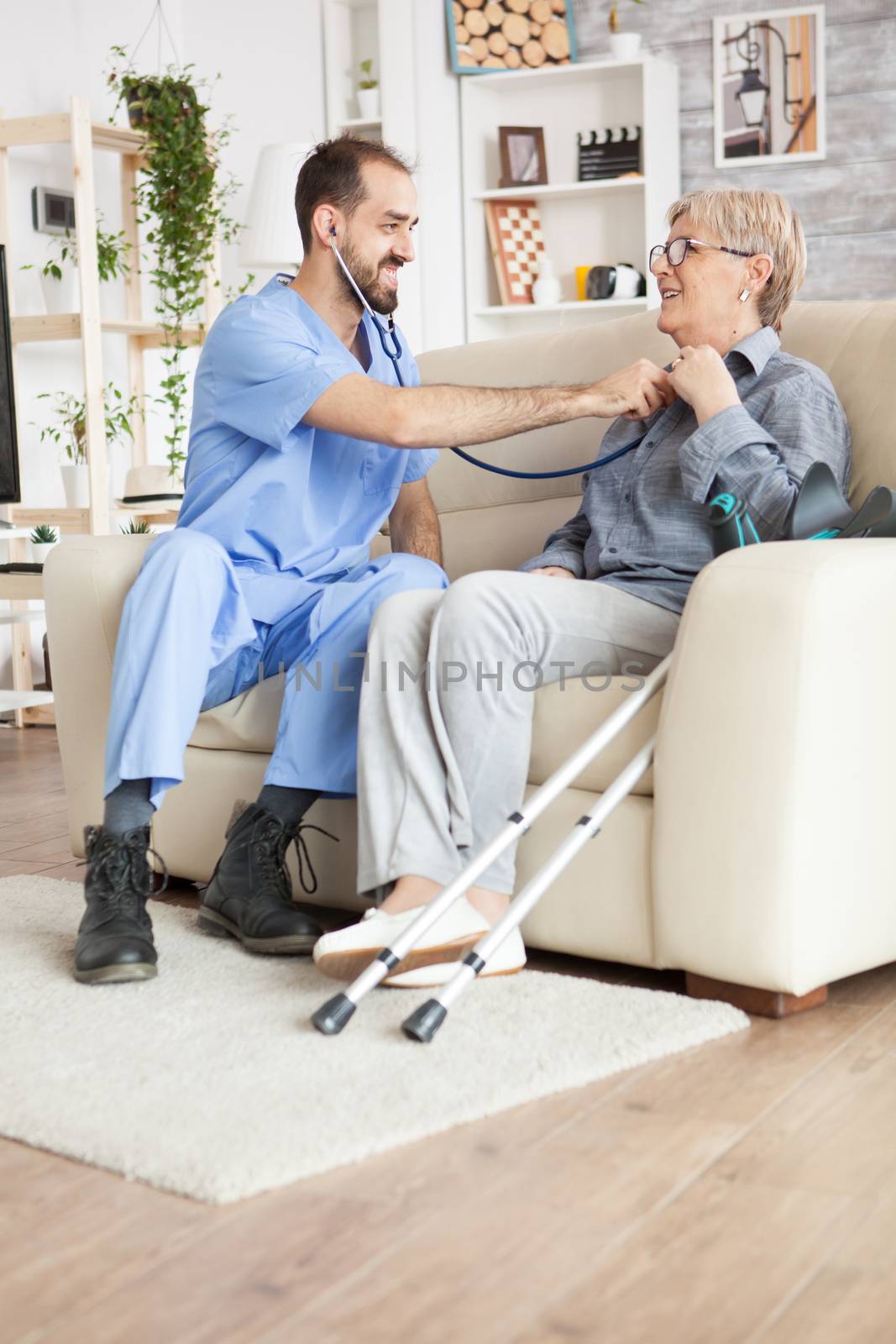 Young doctor using stethoscope to listen old woman heart beat in a nursing home.