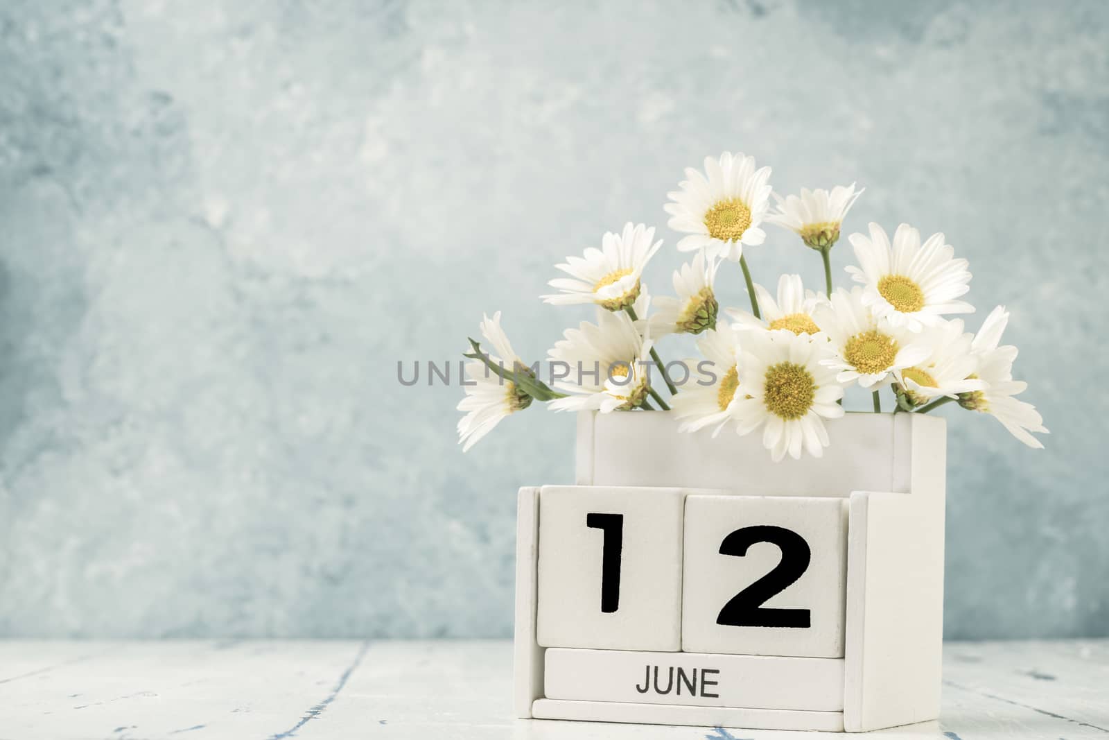 White cube calendar for june decorated with daisy flowers over blue background with copy space