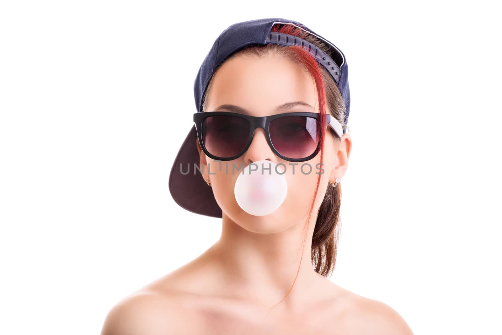 Beautiful stylish girl with backwards snapback cap and sunglasses, blowing a pink bubble with her chewing gum, isolated on white background.
