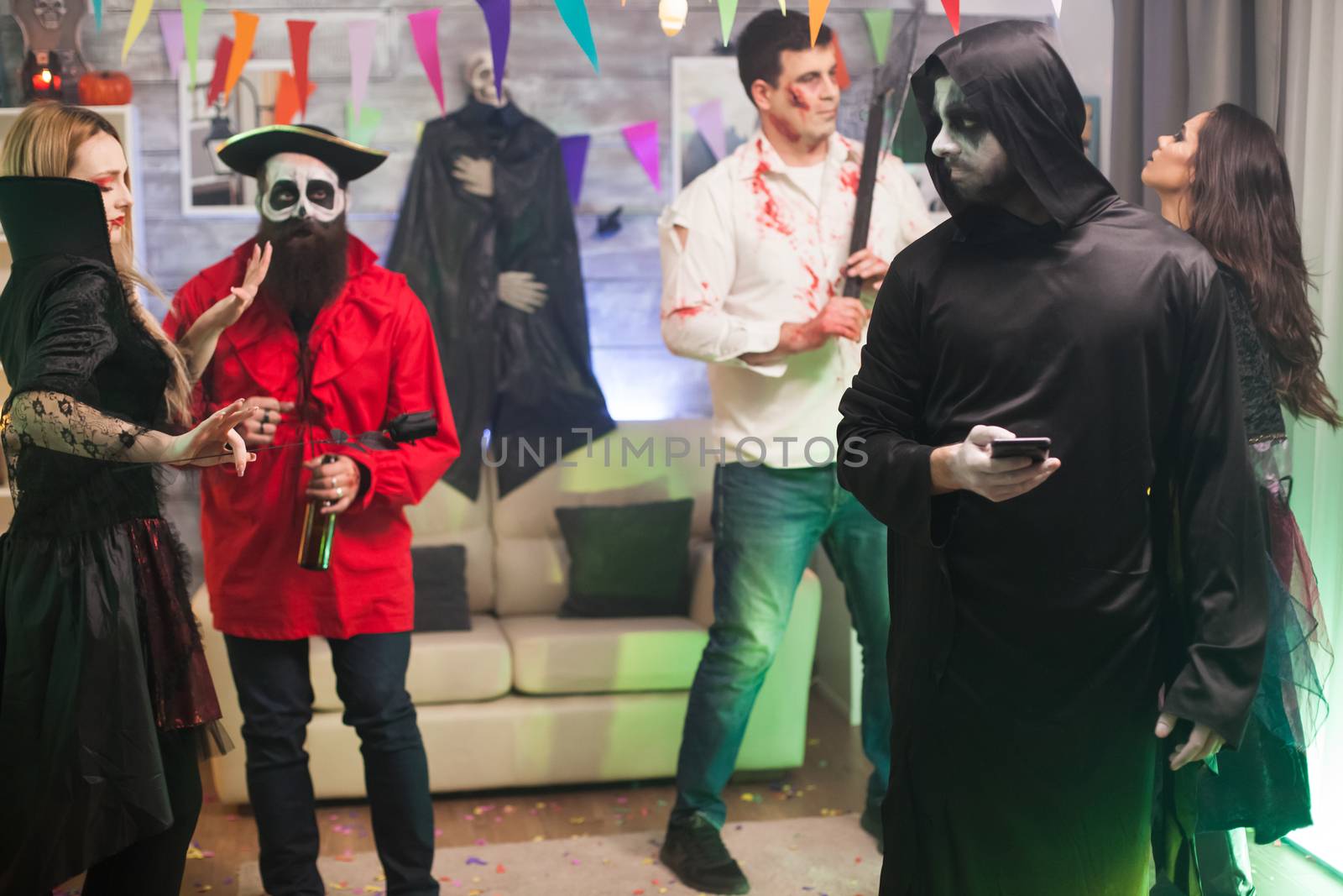 Bored man dressed up like a grim reaper at halloween party using his phone.