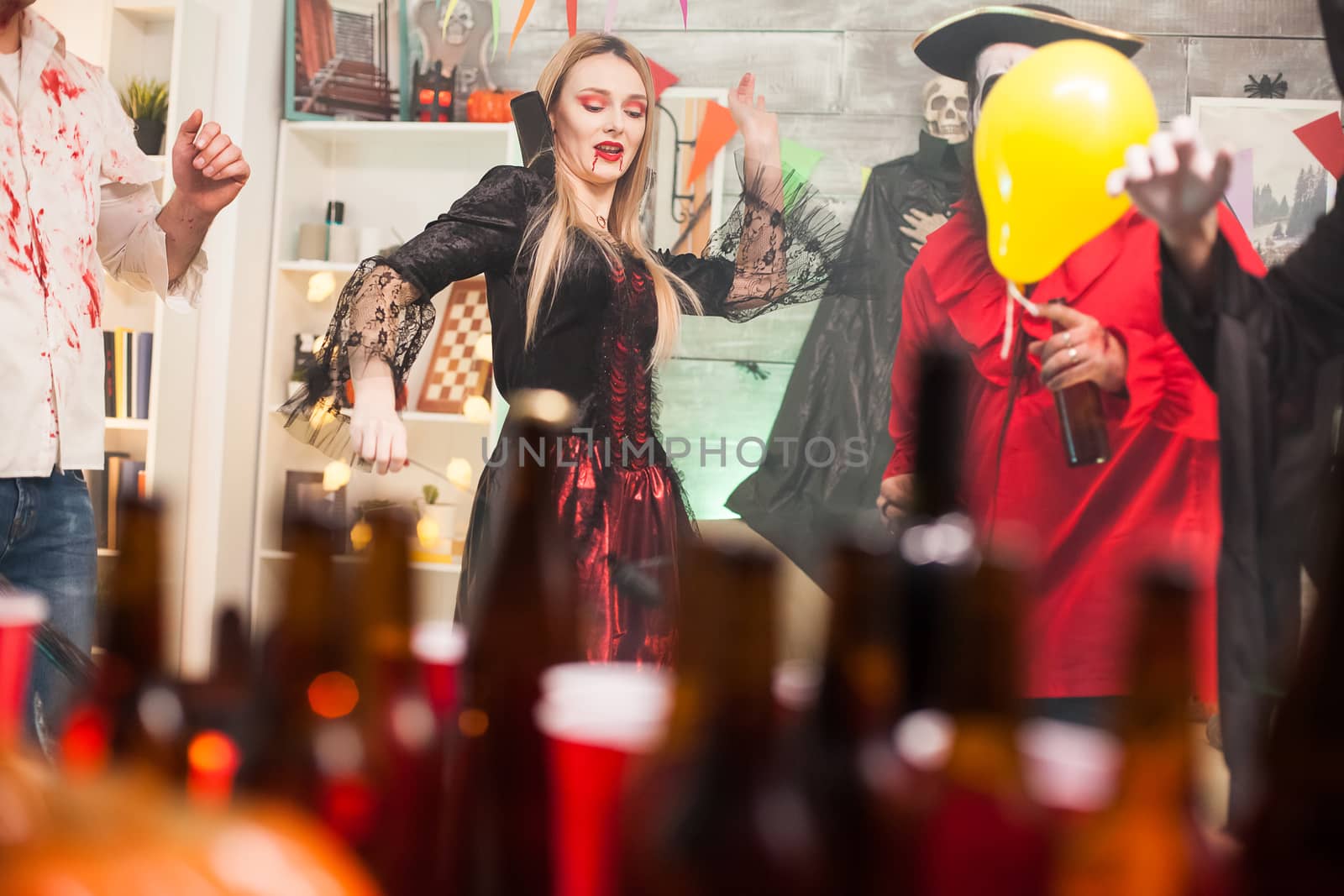 Beautiful young woman dressed up like a vampire showing dancing moves at halloween celebration with her friends.