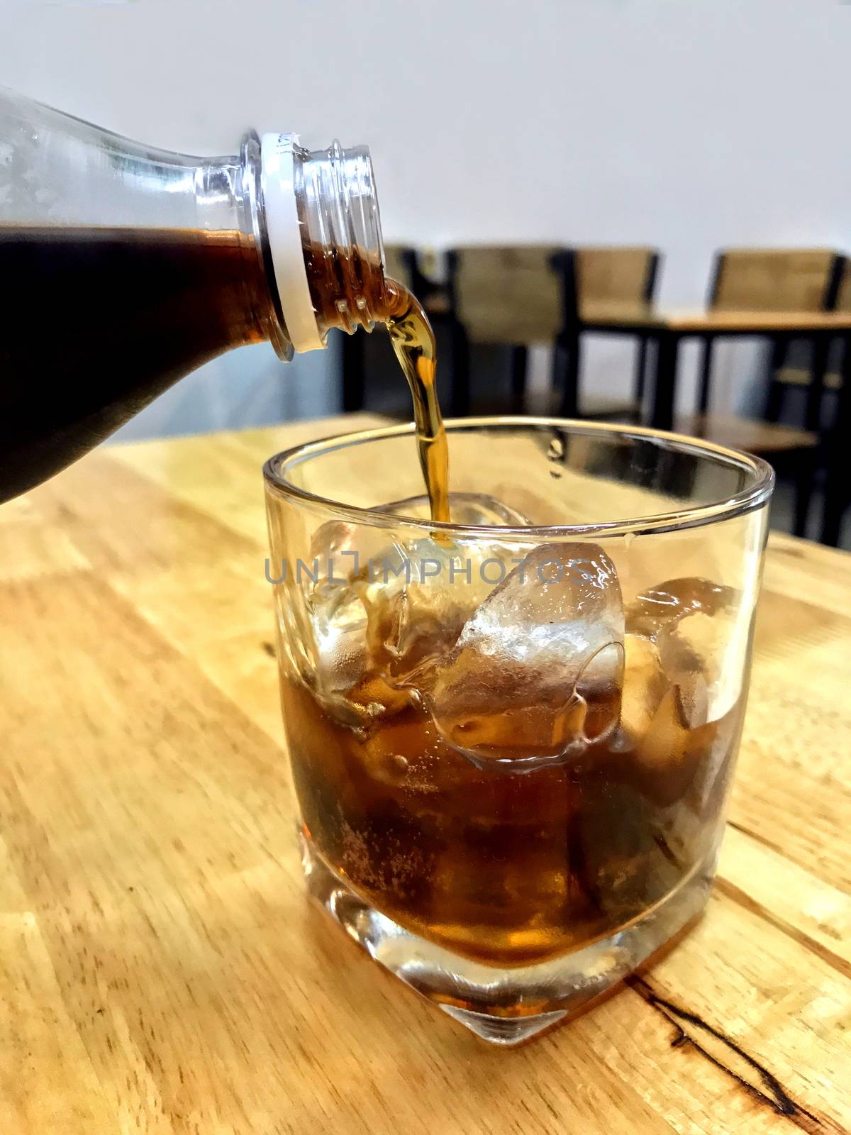 Cola in glass ice, Pouring cola from glass bottles drinks to a glass with ice cubes, cola in glass ice beverage Drinks on the restaurant table