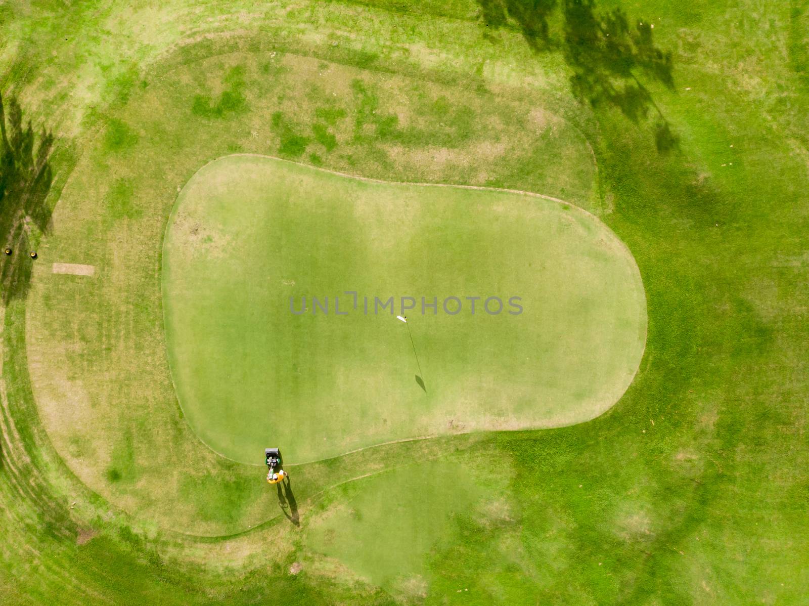 Aerial top view Golf Course, Lush green grass on golf course with path for golf cart, Man cutting the grass with electric lawn mower and flag 