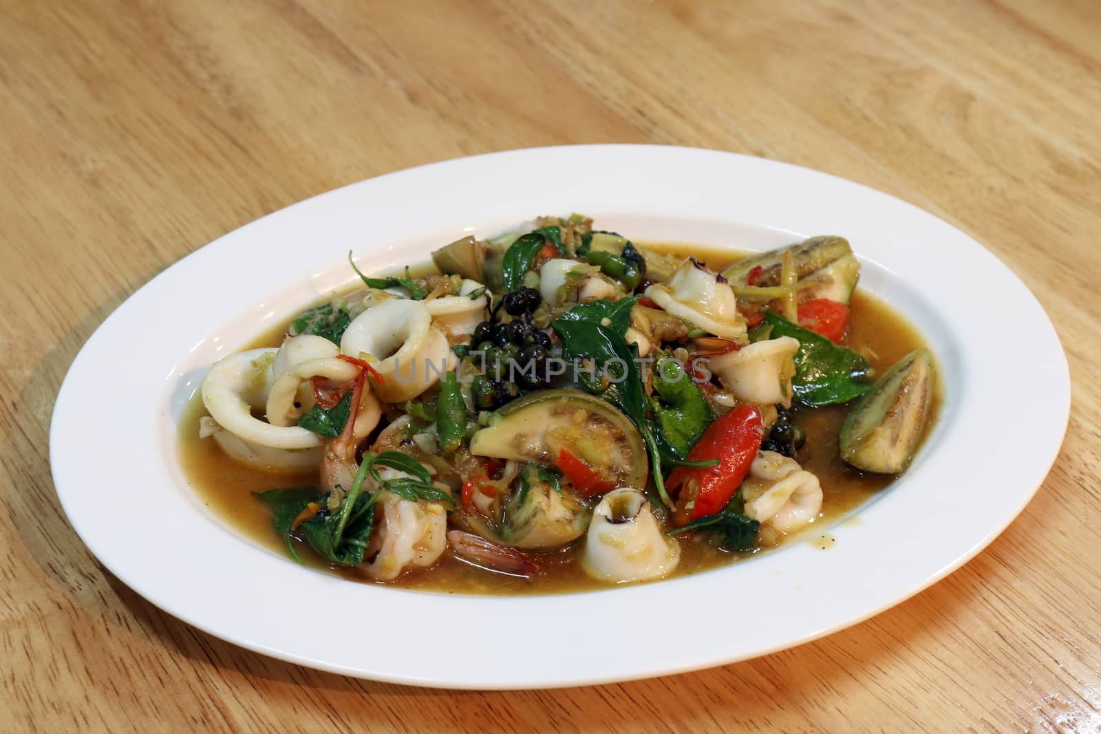 Fried stir sizzle spicy seafood on a white plate - dish at wooden Table, Spicy seafood, Spicy foods, Pad-cha Talay (thai word)