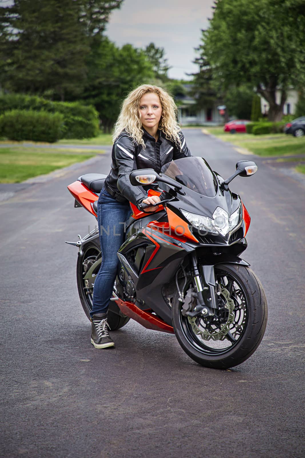 twenty something curly blond woman, sitting on a sport motocycle, in the middle of the road
