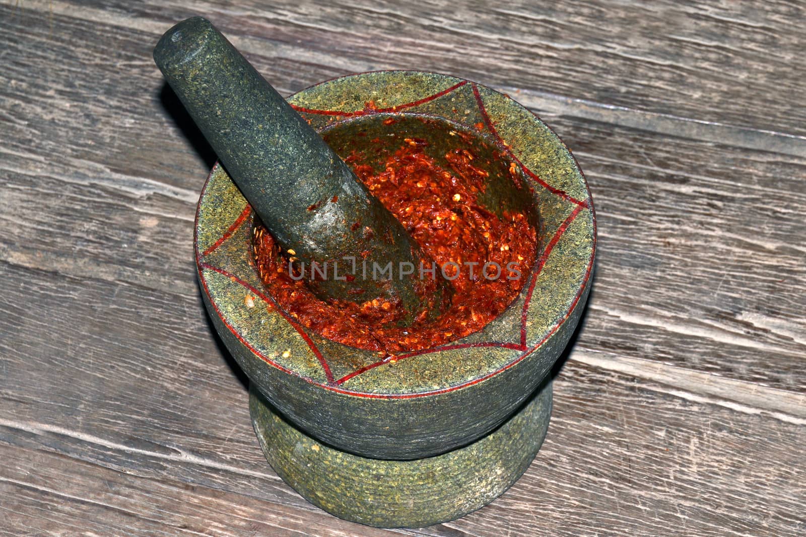 Chili grinding in Mortar stone on wooden background, Mortar and pestle is red chili grinding and garlic for curry ingredients, Thai red curry grinding paste for ingredients sour soup spices in mortar