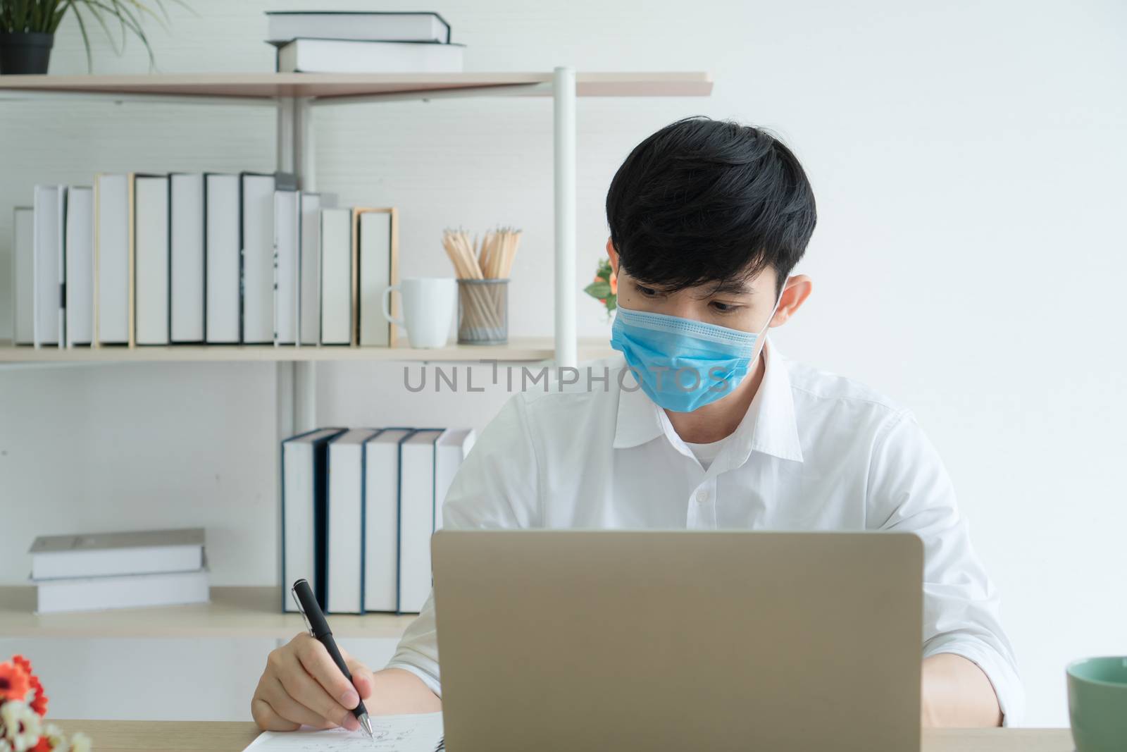 Work from home - Concepts. A young Asian man is happily working at home. He is using a laptop to work. He wears a mask to prevent the outbreak of the virus.