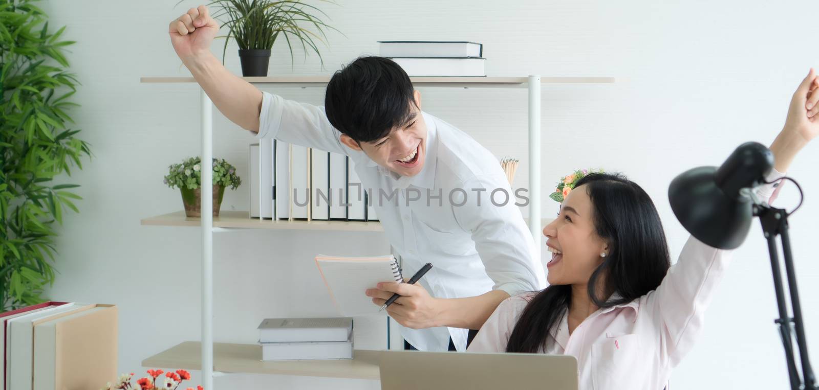 Working from home - Concept. Asian young people are working together at home happily. They are using laptops for work. They have bright, cheerful faces.