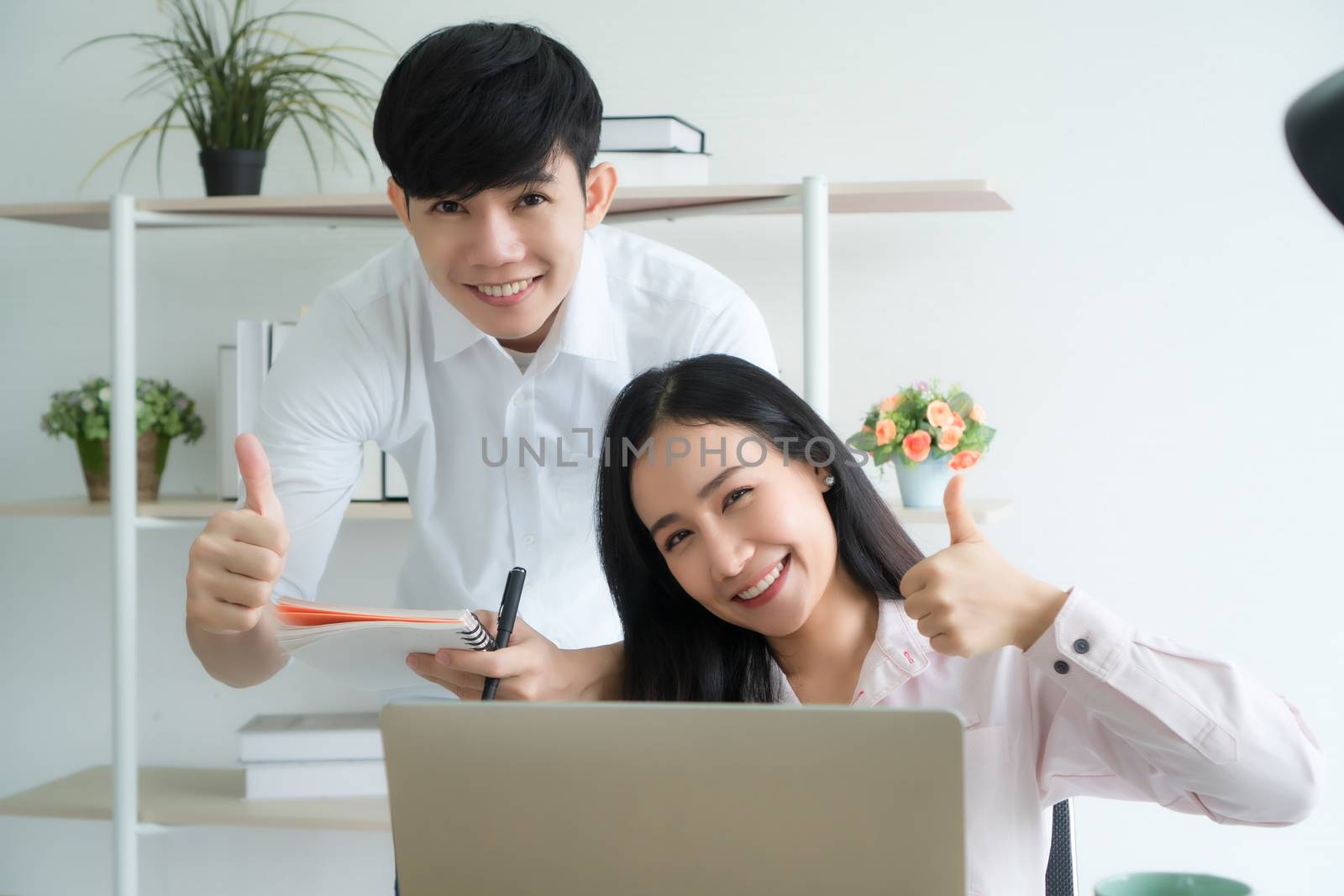 Working from home - Concept. Asian young people are working together at home happily. They are using laptops for work. They have bright, cheerful faces.