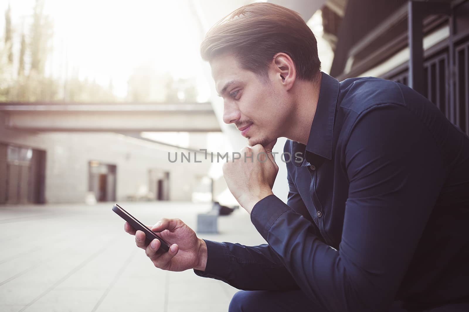 Smiling businessman use a smartphone at street.