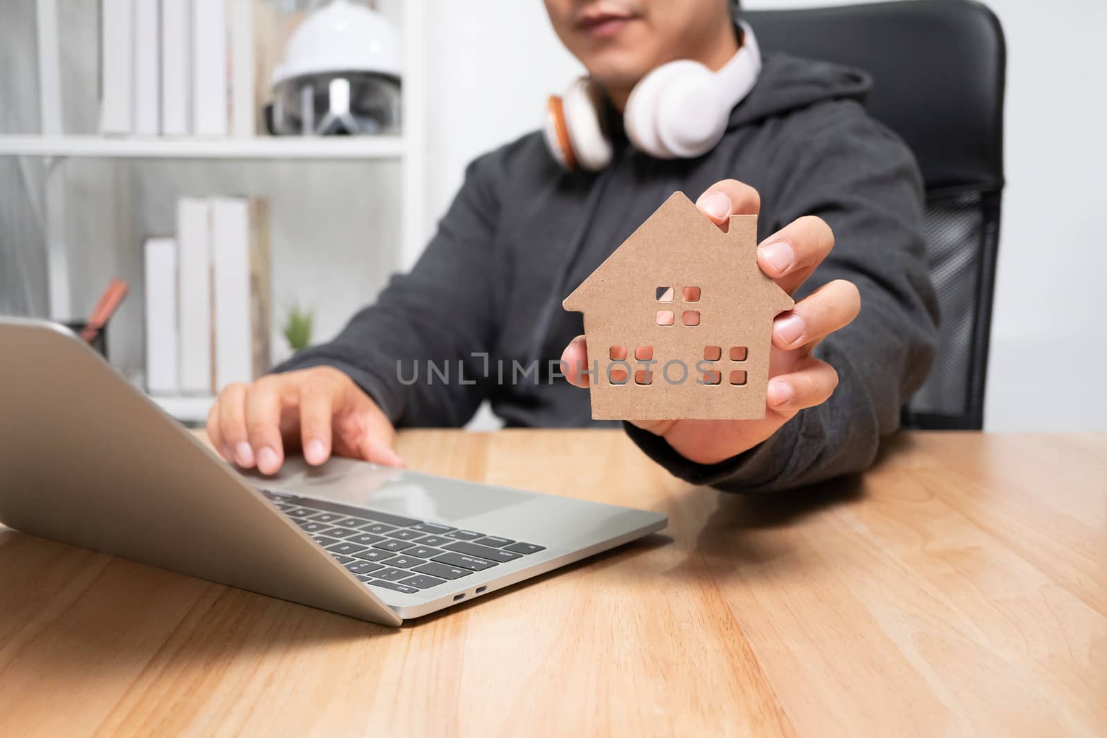 Smiling businessman holding a wooden house in home workspace. The concept of working from home until the end of Coronavirus (COVID-19) quarantine, happily freelance working lifestyle by PattyPhoto