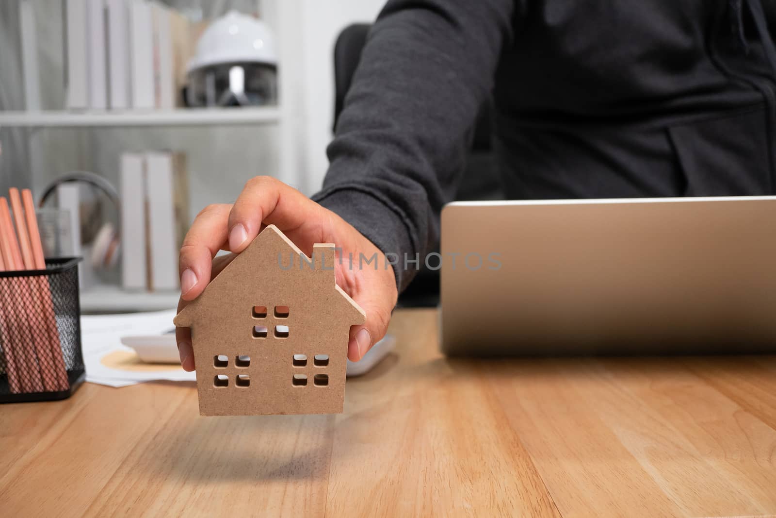 Smiling businessman holding a wooden house in home workspace. The concept of working from home until the end of Coronavirus (COVID-19) quarantine, happily freelance working lifestyle