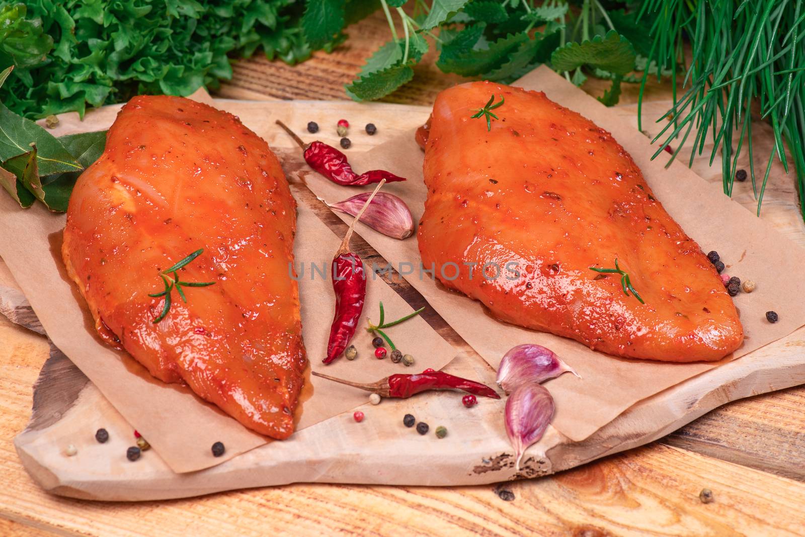 Marinated Chicken Breast with spices rosemary and vegetables on a cutting board and on a wooden table. Top view. Tasting diet meat.Chicken meat closeup. Raw meat in marinade. by nkooume