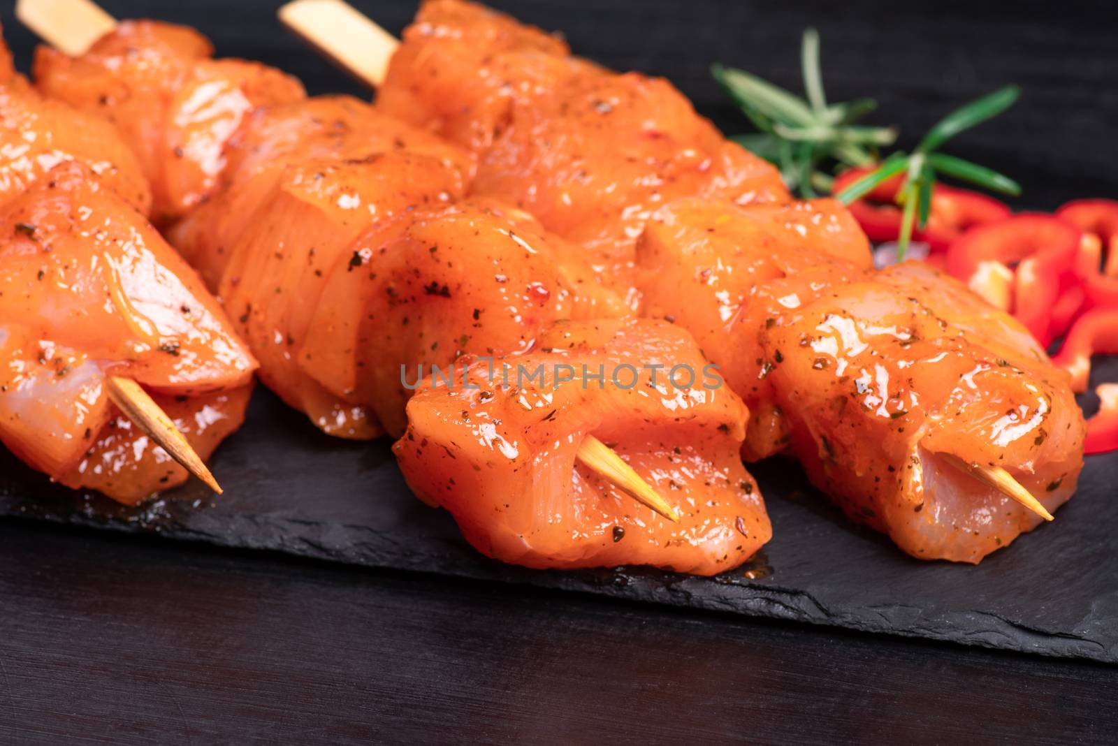 Raw marinated and spicy chicken skewers.Raw chicken skewers in marinade with spices on a black plate and on a wooden table. Top view. Chicken meat close up. Raw meat in marinade. Tasting diet meat. by nkooume